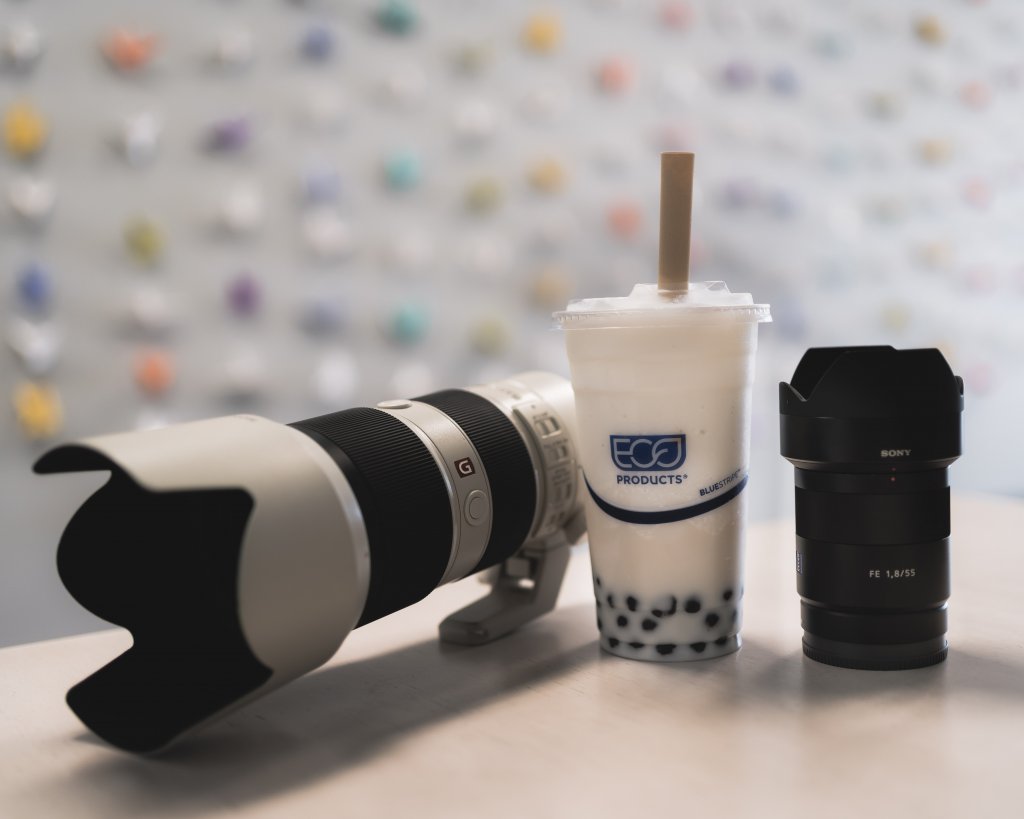 picture of 2 camera lens and a almond milk tea with boba in between in front of a origami crane wall